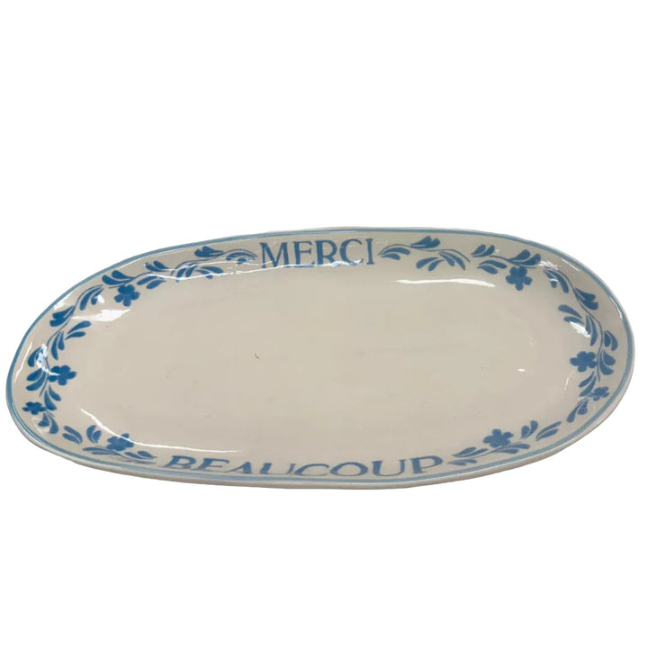 White ceramic platter with blue floral design and 'MERCI BEAUCOUP' text on a white background.